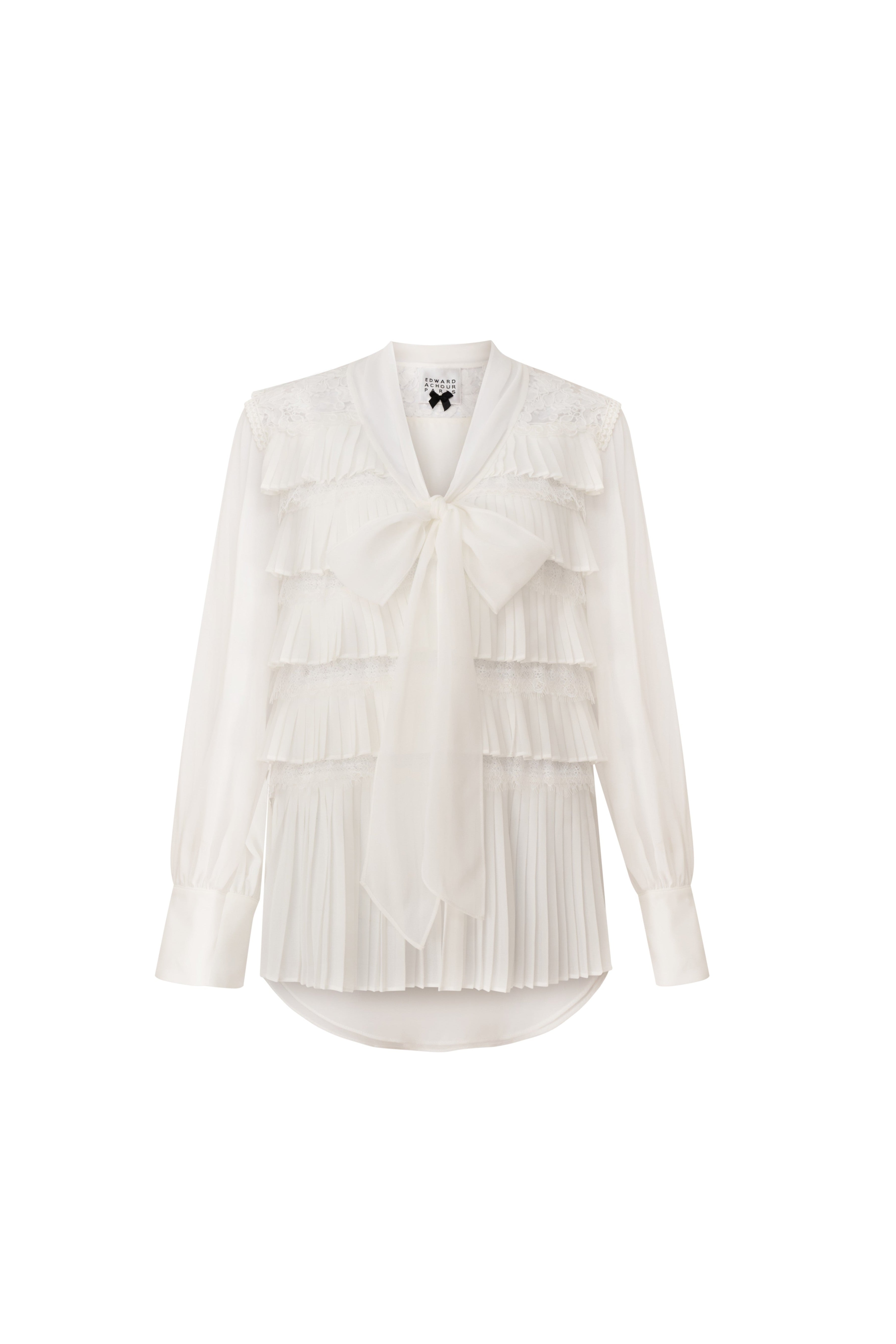 Front view of a white long-sleeve blouse with tiered pleats, lace panels, and a large bow by Edward Achour Paris.
